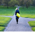A woman walking down a path with a yellow bag.