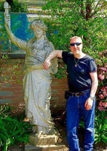 A man standing next to a statue in a garden.