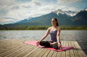 A woman doing yoga on a dock near a lake.