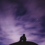 Silhouette of a person sitting on top of a rock at night.